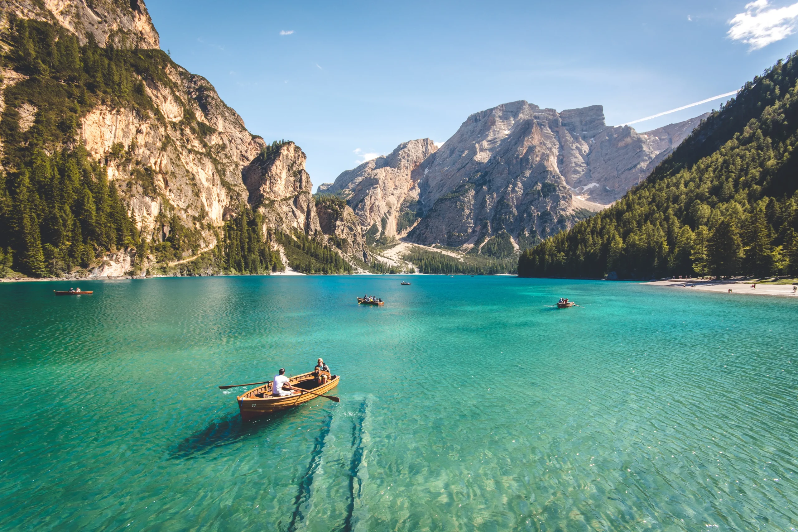 Ein Ruderboot, dass auf einem türkisblauen See treibt in Richtung von Bergen und einem strahlend blauen Himmel als Symbol für die Suche nach Sinn